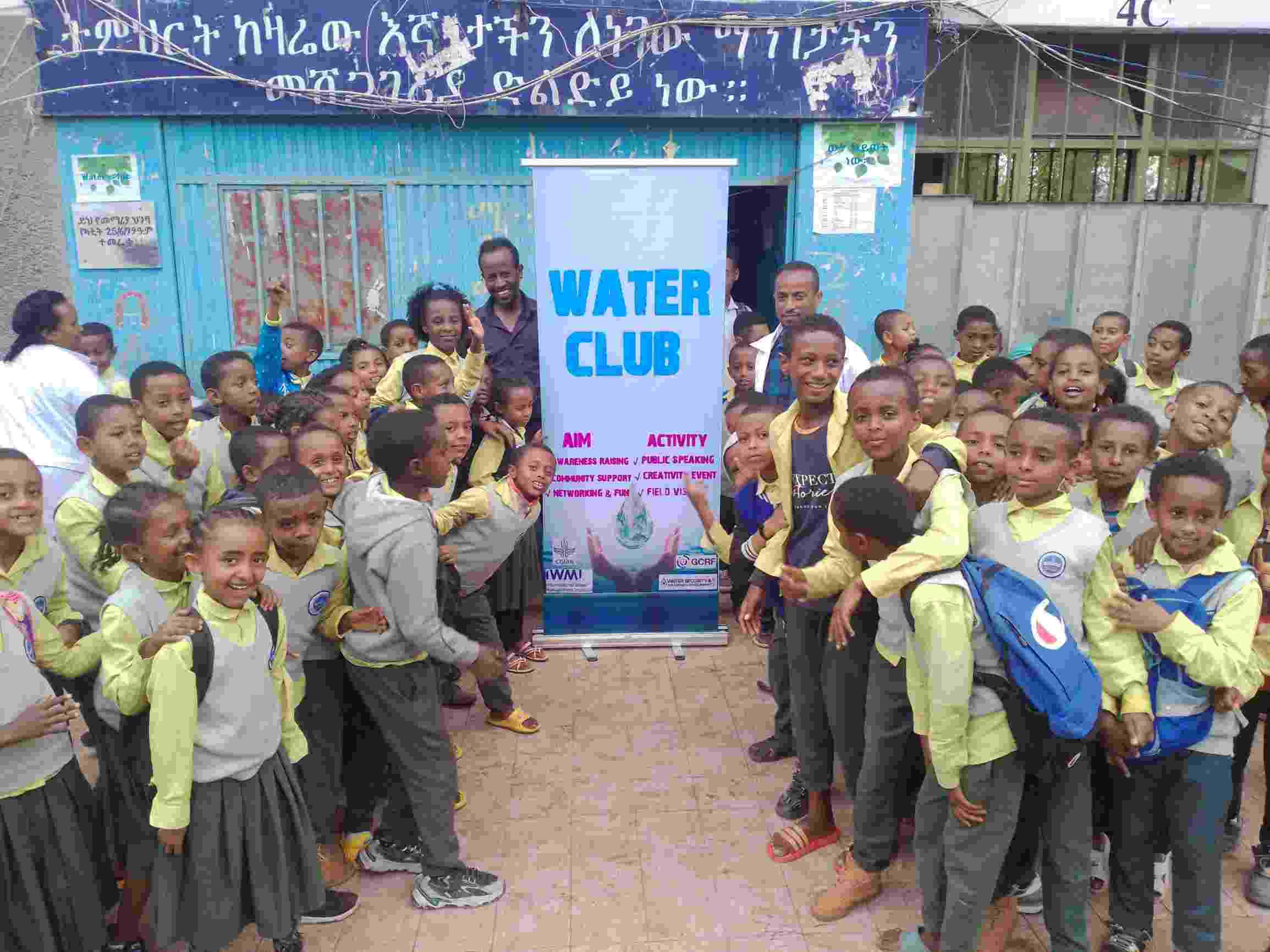 A large crowd of school pupils stand together with Hub researchers around a banner that reads 'Water Club', smiling at the camera